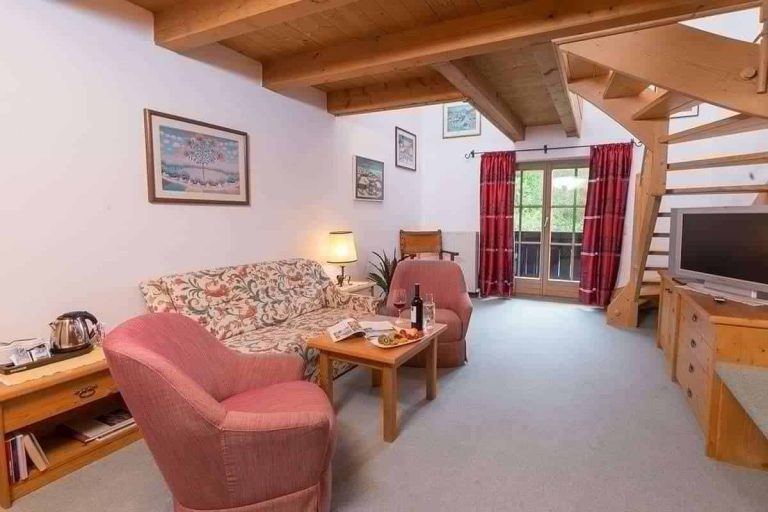 Gemütlicher Wohnbereich mit rustikaler Holzdecke, Sofas und Balkon, ideal für Entspannung im Erlhof.
