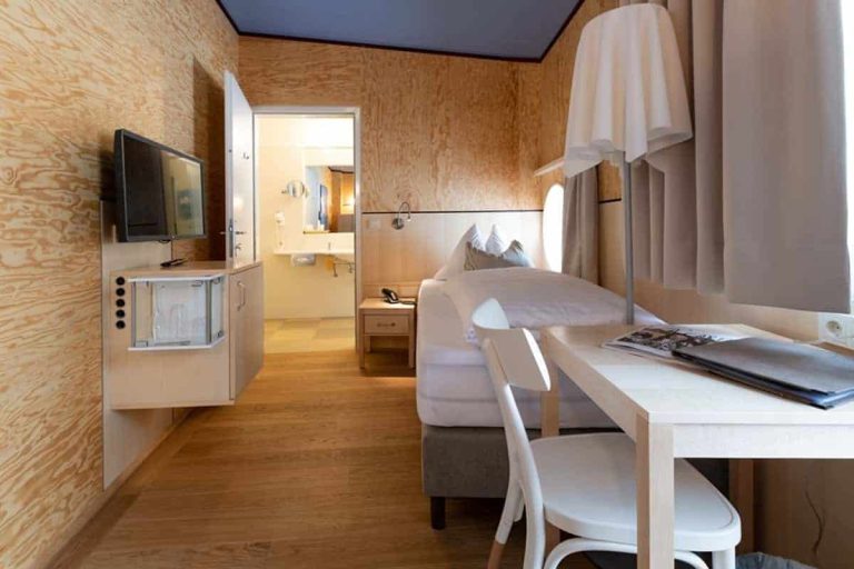 Modernes Zimmer im Hotel Erlhof mit TV, Tisch und Blick ins Badezimmer.